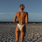 Woman in a white bikini standing on a sandy beach with a clear blue sky.