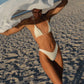Woman in a white bikini standing on a sandy beach with a large piece of fabric.